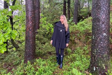 Blæst Bergen Poncho i svart med hette og frontlomme, designet for komfort og beskyttelse mot regn og vind.